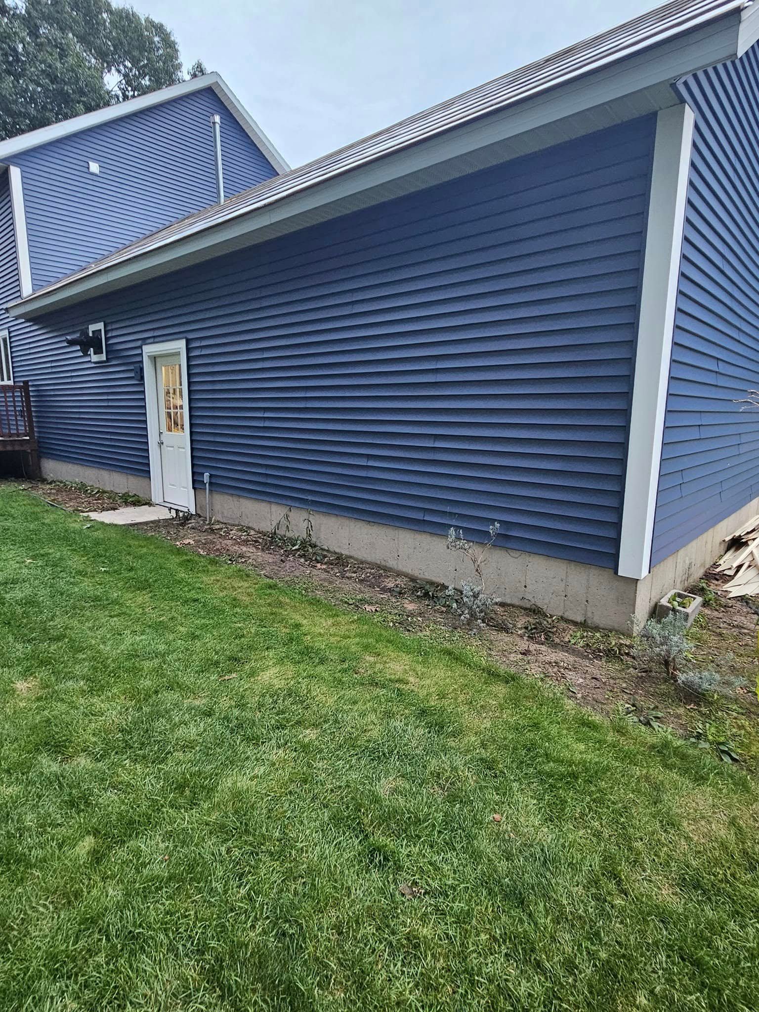 Blue-sided building with a white trim, a small door, and a grassy lawn in front.