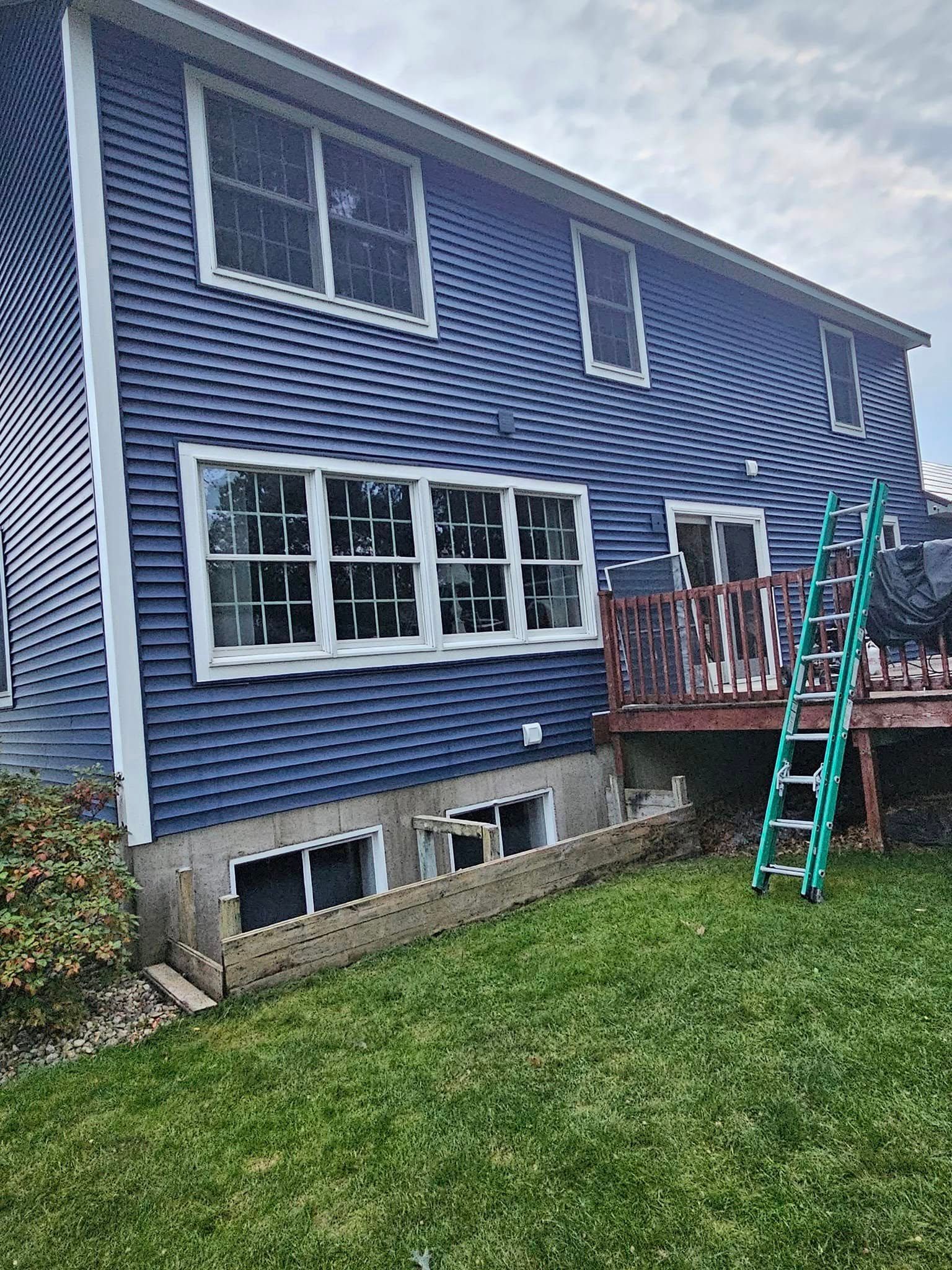Blue two-story house with a small deck and green ladder in the backyard