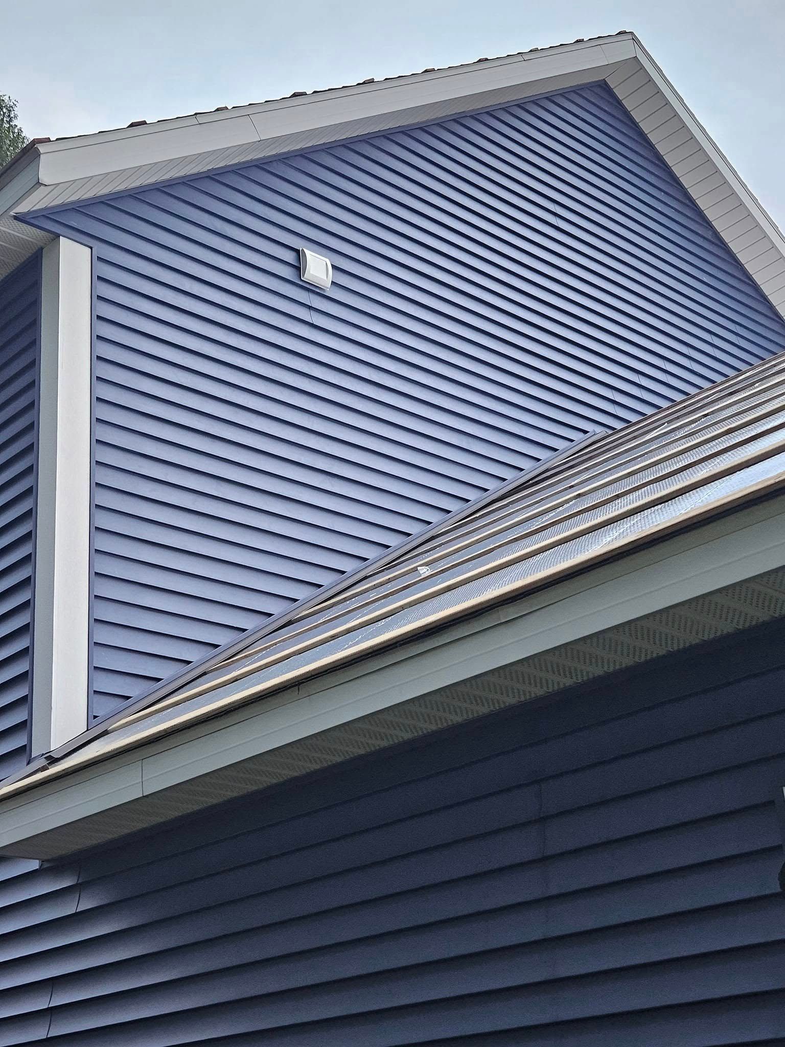 Blue vinyl-sided house exterior with white trim and sloped roofline