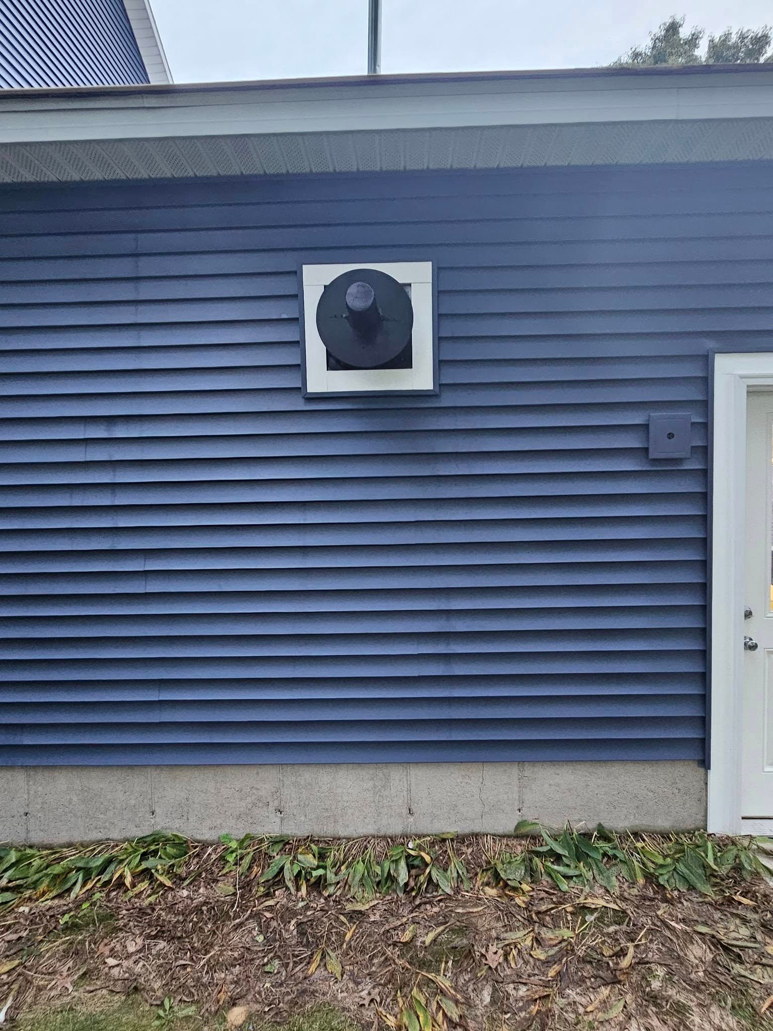 Blue house exterior with a round vent centered on the wall and a white door edge on the right.
