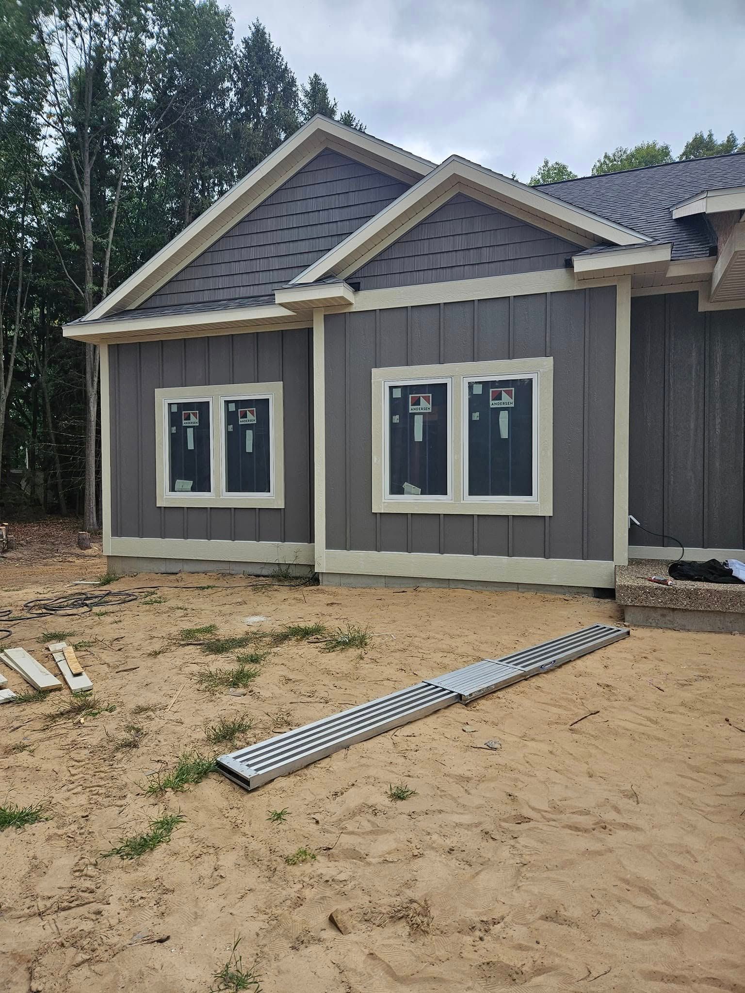 Partially finished gray house with white trim and sandy yard, viewed from the front