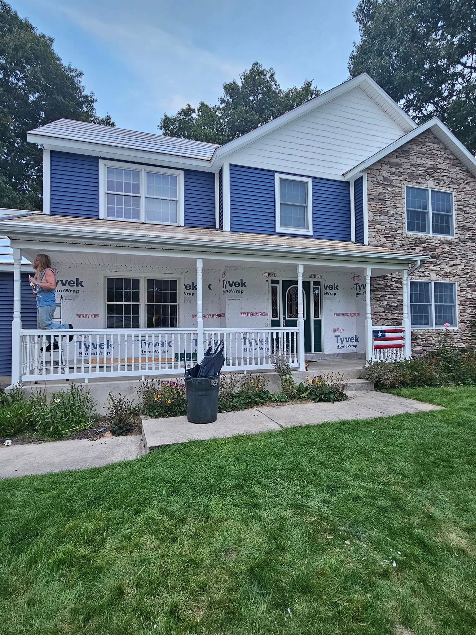 Blue two-story house with white trim, front porch, and green lawn under a cloudy sky