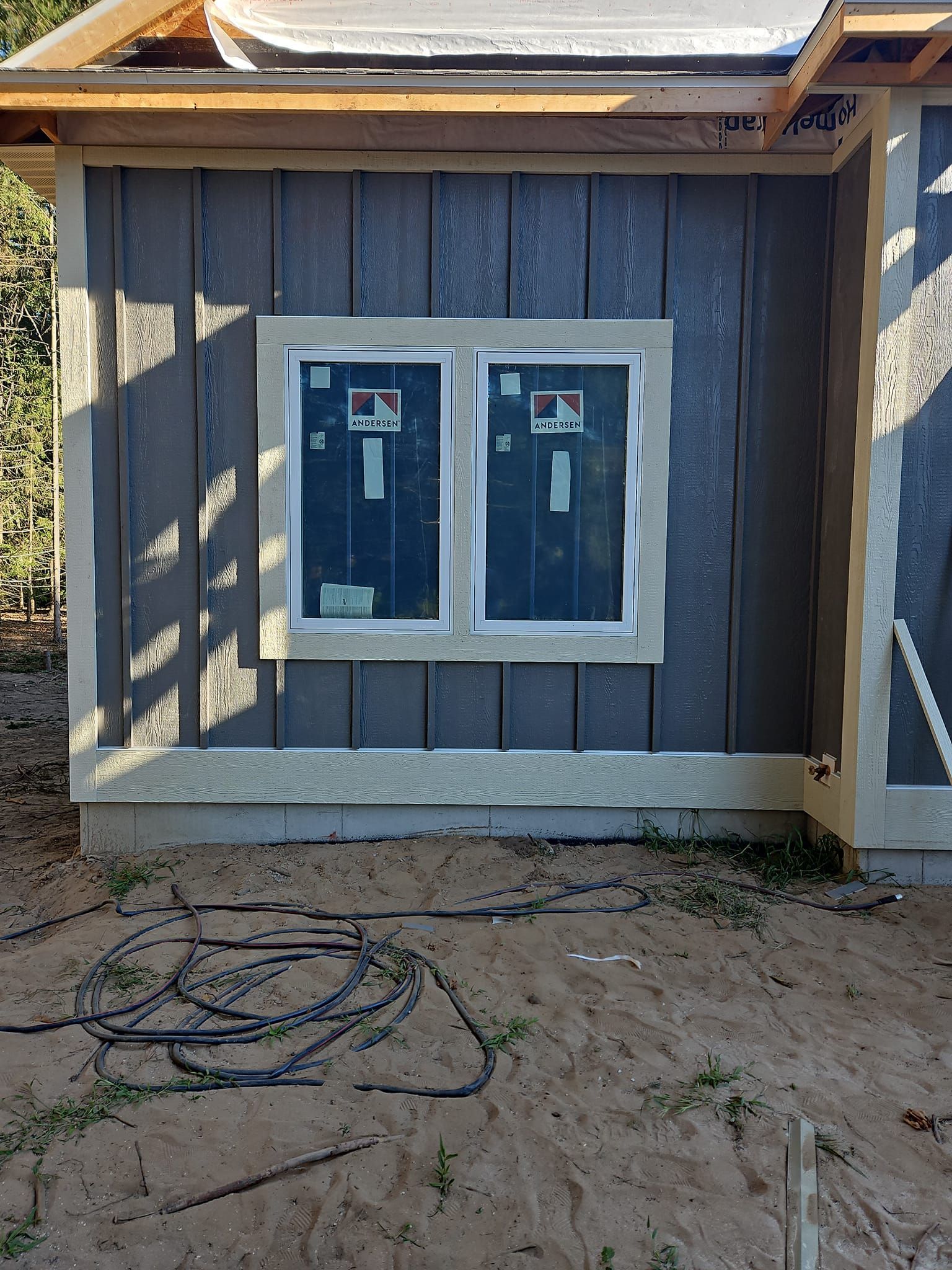 Exterior wall under construction with two white-framed windows and unfinished siding.
