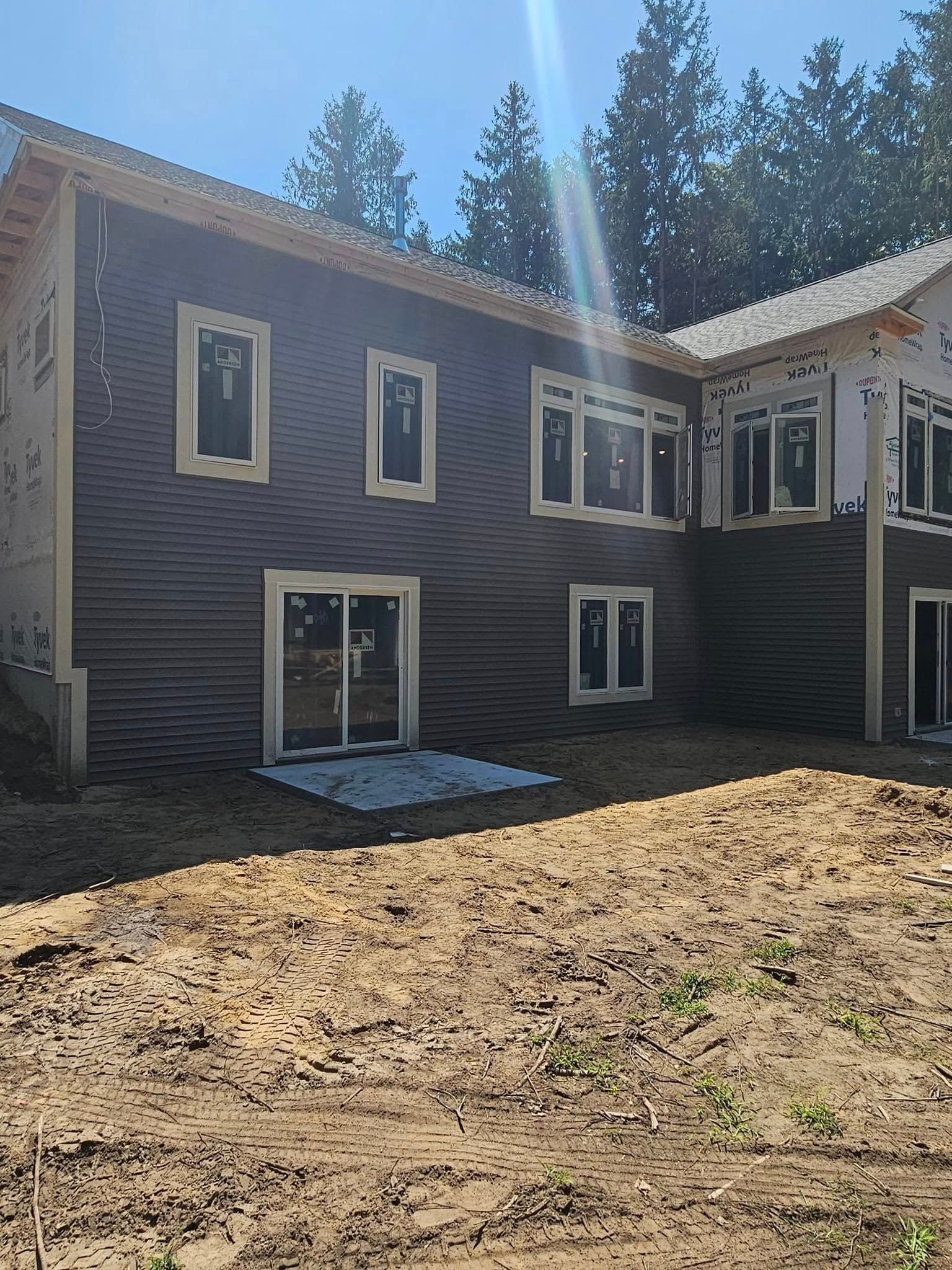 Two-story gray house exterior with white-trimmed windows and a dirt yard in front.