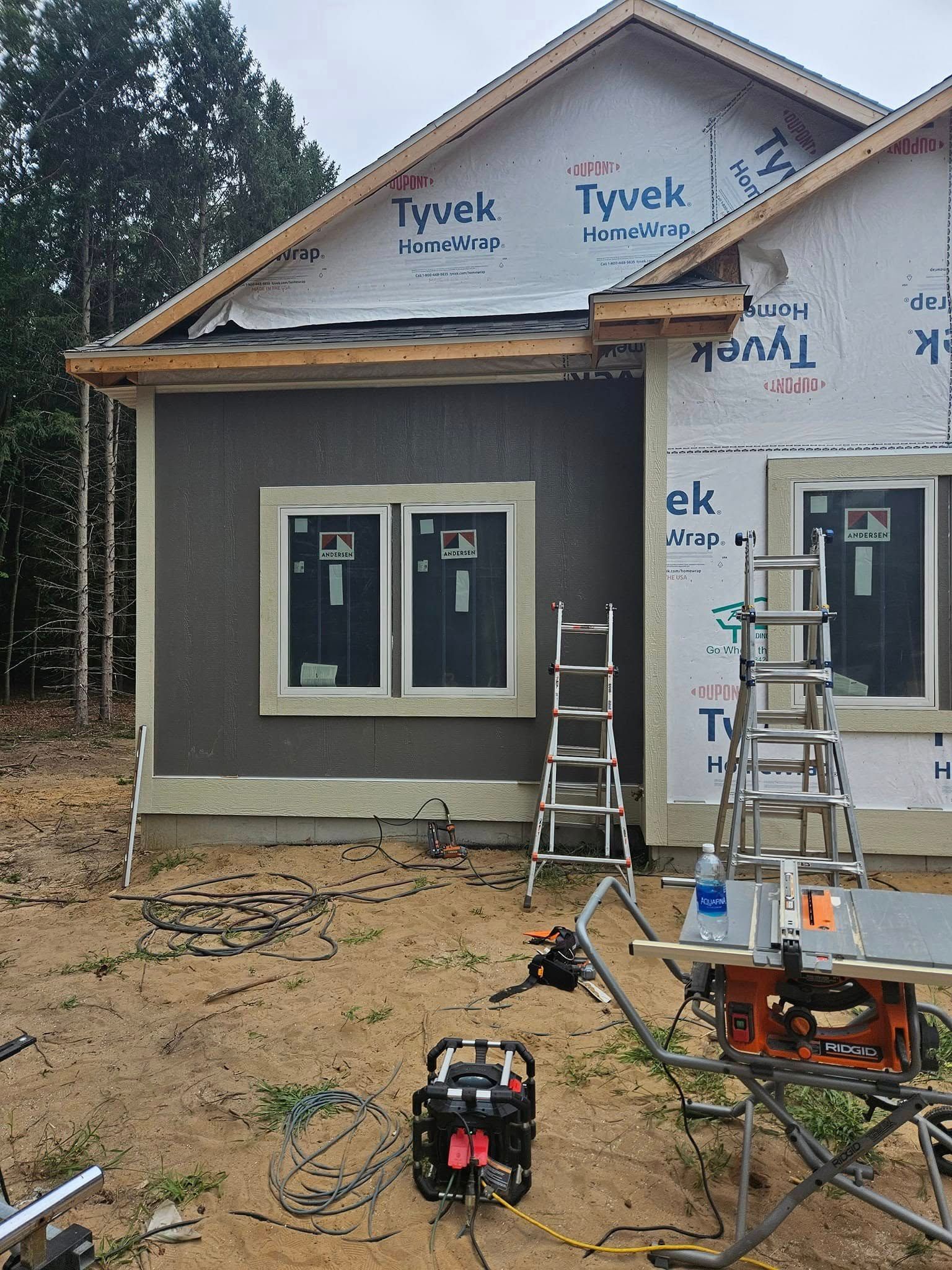 Partially built house with Tyvek wrap, ladders, and construction tools in a muddy yard