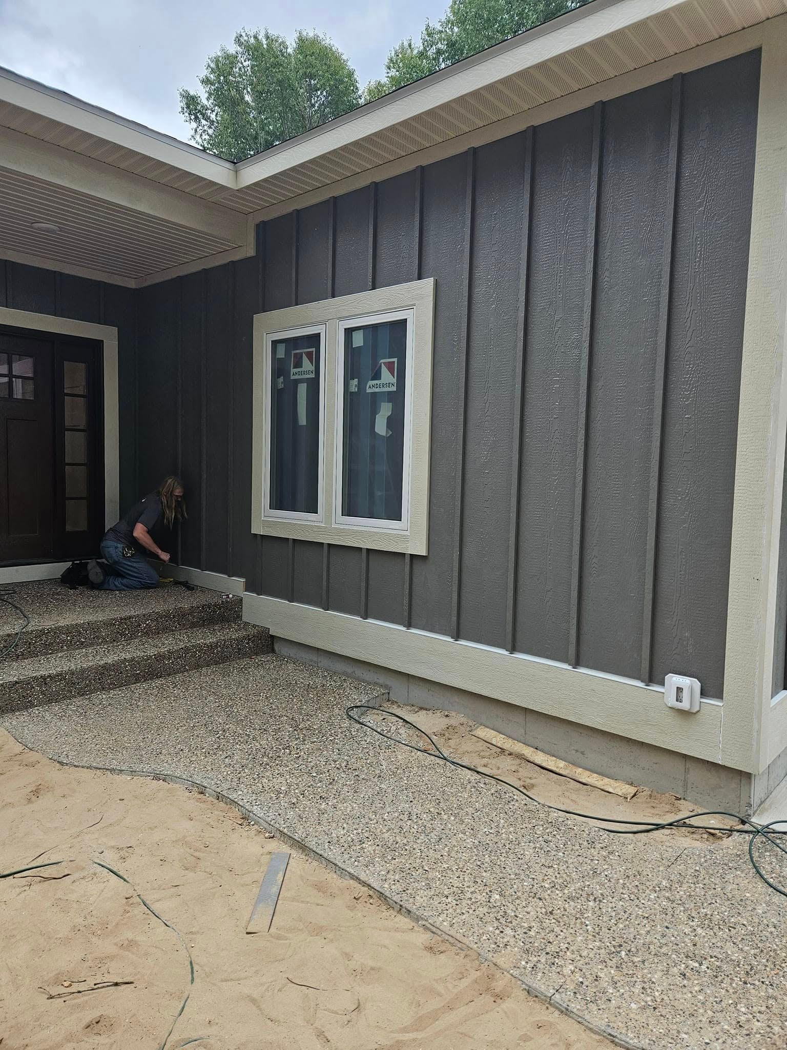 Gray house exterior with white-trimmed window and a person crouching by the front steps