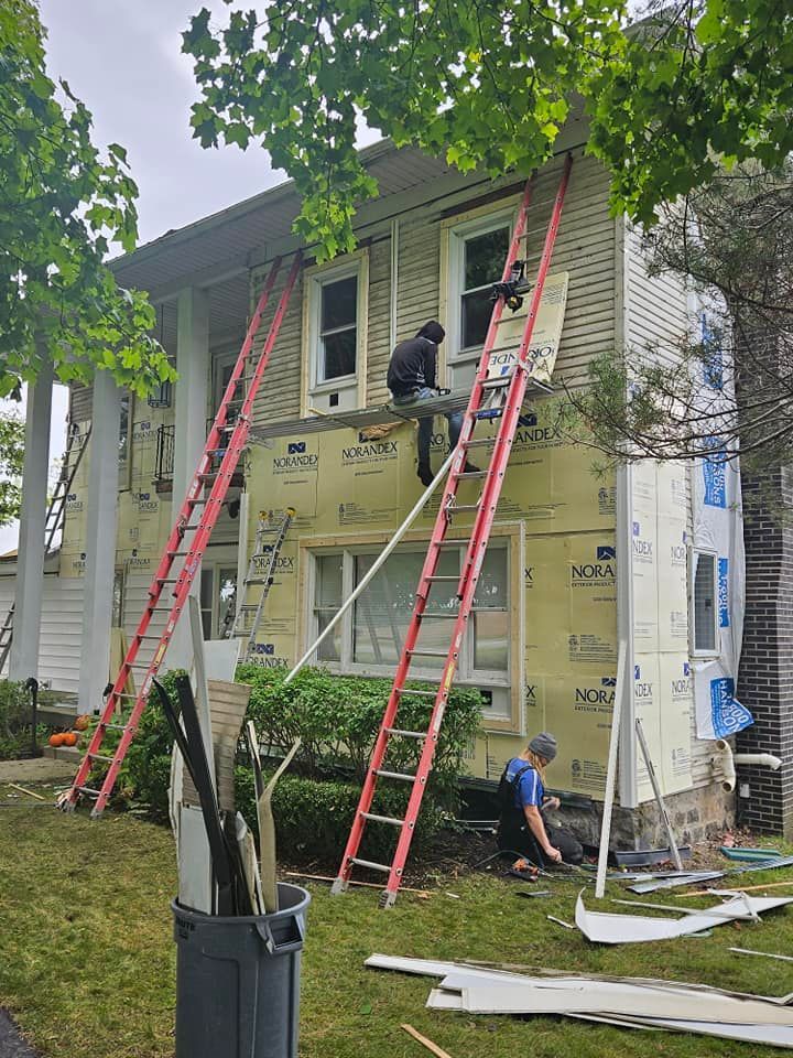 Workers on red ladders painting a house exterior with green trim and yellow underlayment.
