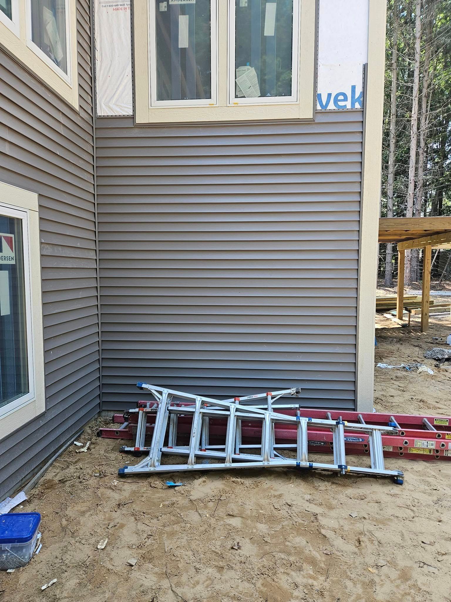 Ladder lying on dirt beside a house with gray siding and windows, near a partially built outdoor area