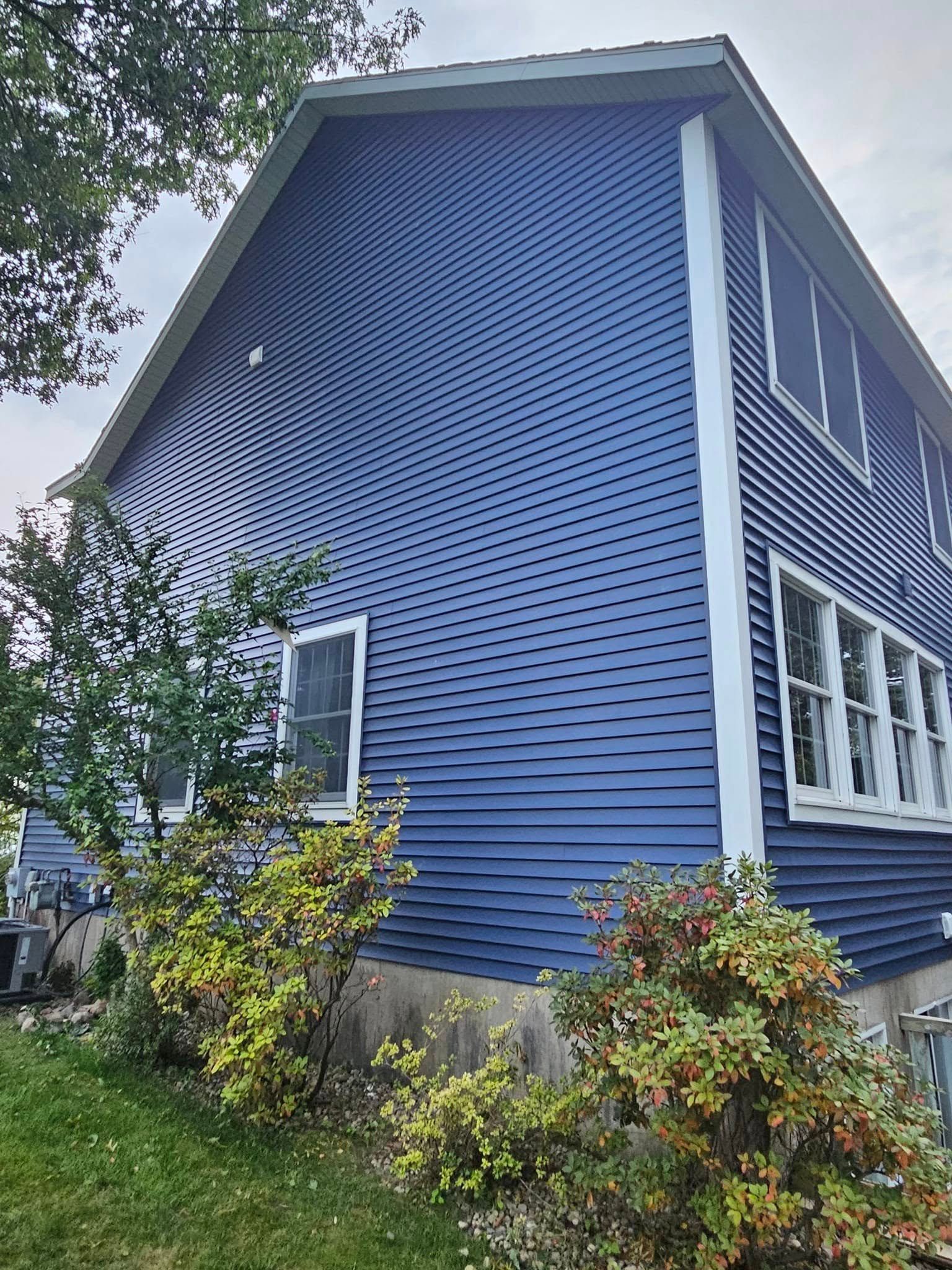 Blue two-story house with white trim and lattice siding, seen from the side amid shrubs and trees.