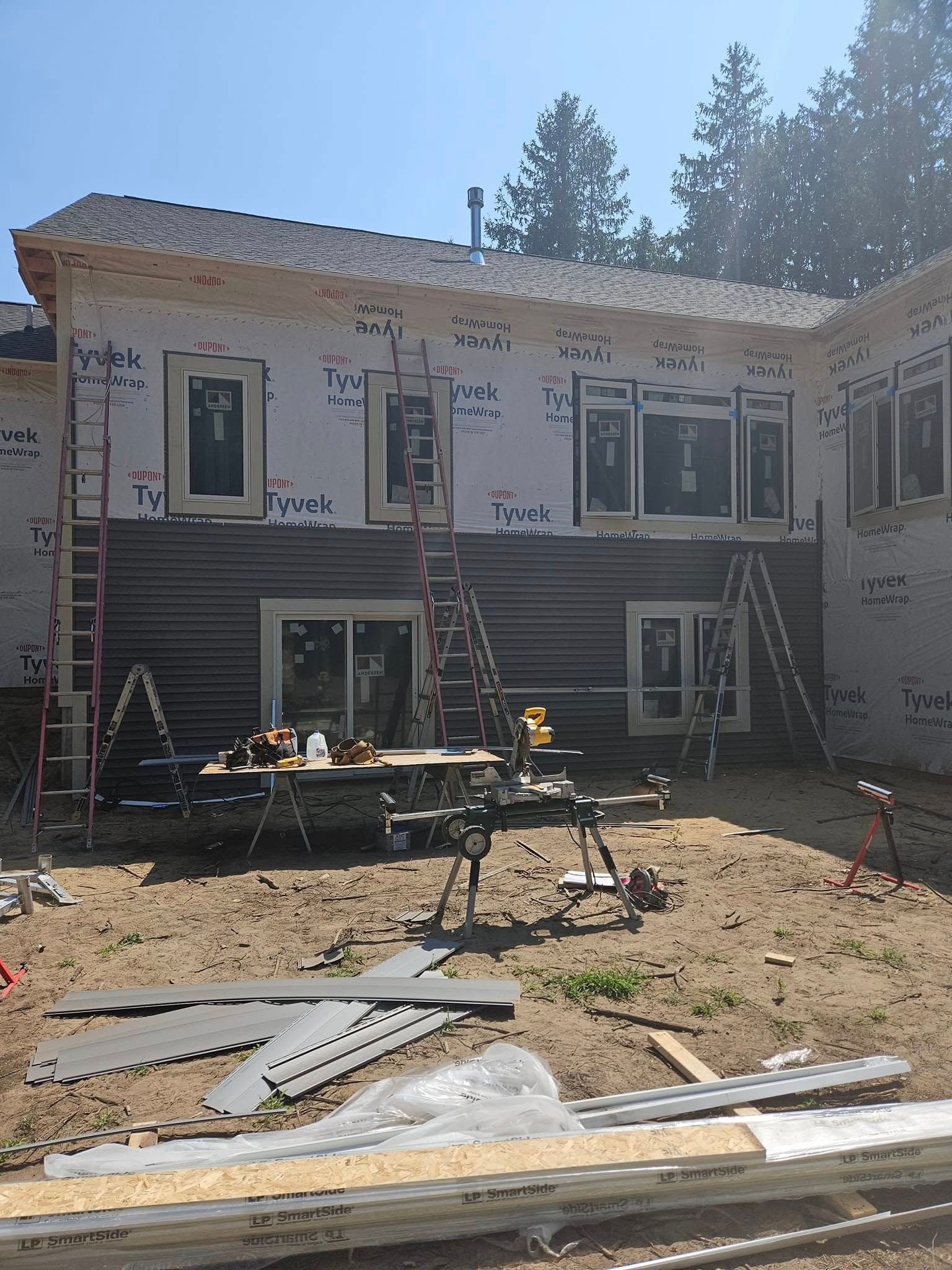 Backyard house under renovation with new siding, construction materials, and tools in front
