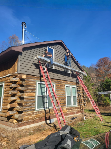 Two workers on ladders repairing the roof and siding of a log cabin under a blue sky.