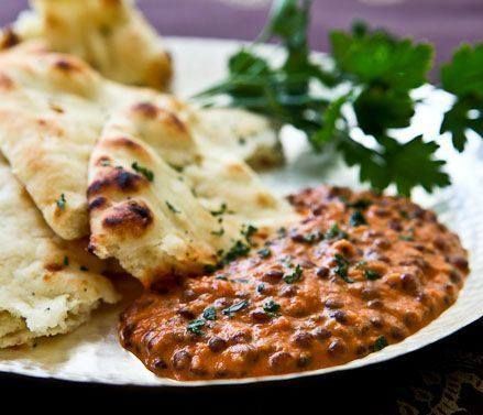 Naan bread with a creamy, dark-colored lentil dish garnished with herbs, on a plate.