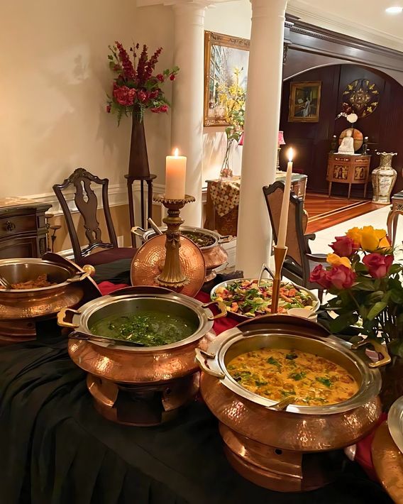 Buffet table with copper serving dishes, candles, and floral decorations.