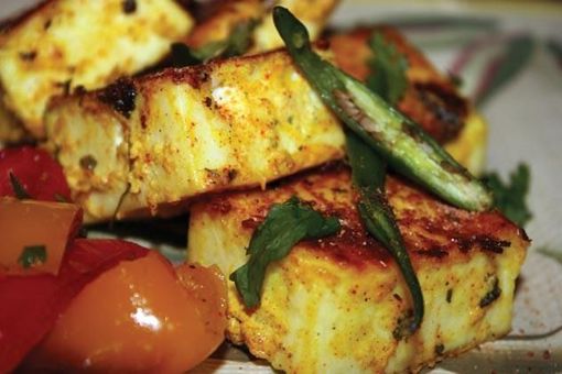 Plates of Indian food: fritters, puffed rice snack, red and green chutneys, fork, on a table.