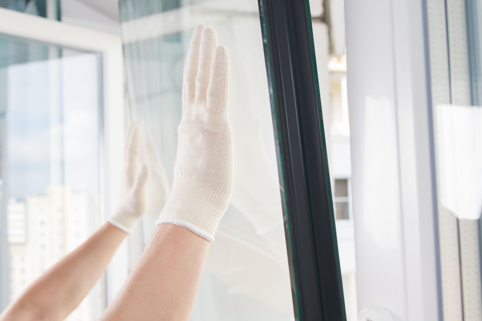 Gloved hands of a craftsman install glass in a plastic window frame. Gloved hands of a craftsman install glass in a plastic window frame.