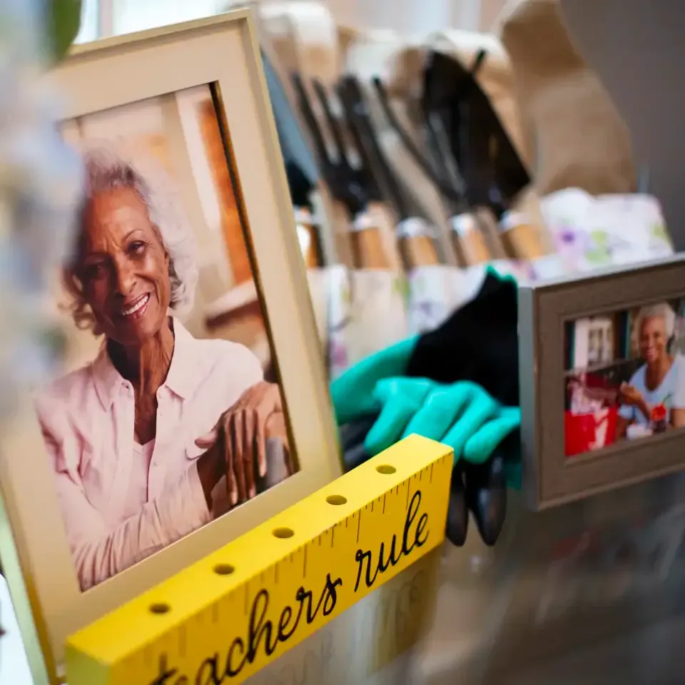 Decorated desk with framed photos, makeup brushes, teal gloves, and a yellow “Teacher’s rule” block