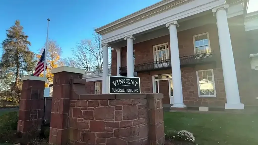 Brick funeral home with white columns and a Vincent sign by the entrance, under a clear blue sky
