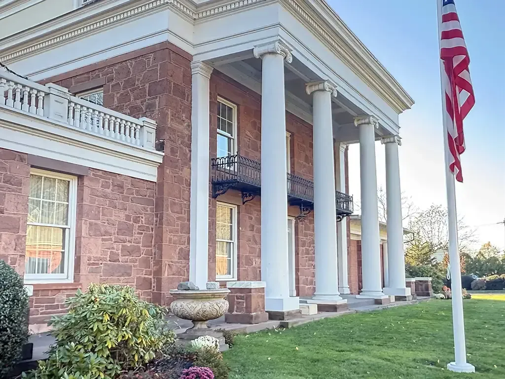 Brick building with white columns and an American flag, viewed from a grassy lawn.