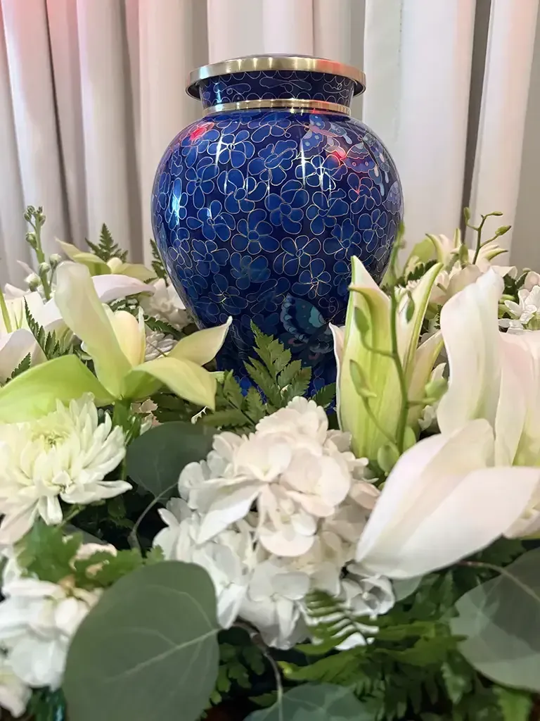 Blue urn surrounded by white lilies and flowers on a floral arrangement