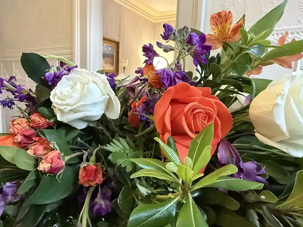 Assorted colorful flowers in a bouquet, including white, orange, purple, and pink blooms, with green leaves.