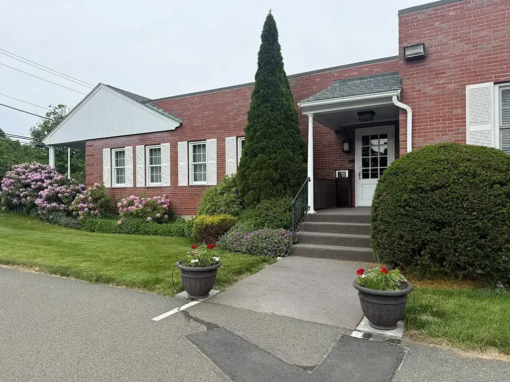 Brick building with white shutters, front entrance, and potted plants along a walkway