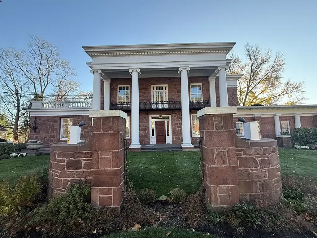 Front view of Vincent Funeral Home with white columns behind a stone entrance gate and lawn