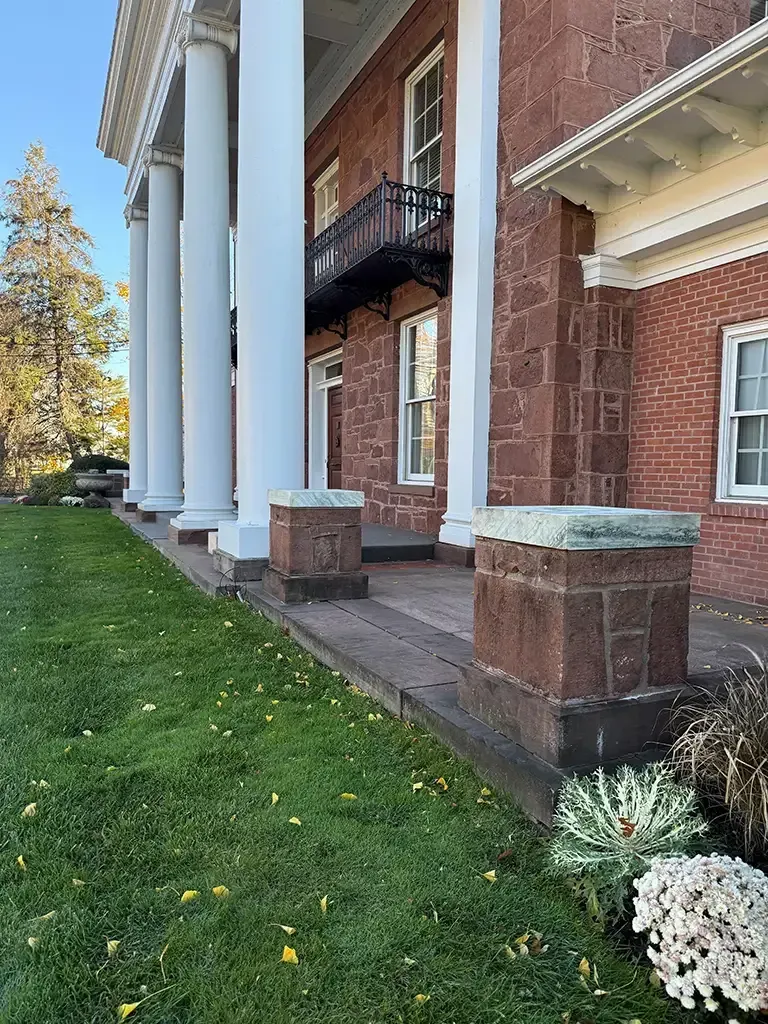 Brick building with white columns, black balcony, and a green lawn in front.