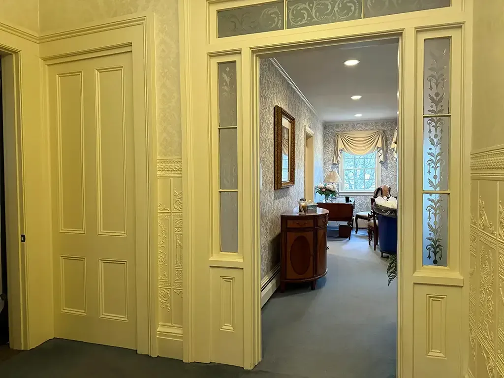 Elegant hallway with cream paneling and frosted glass doors leading to a softly lit room beyond