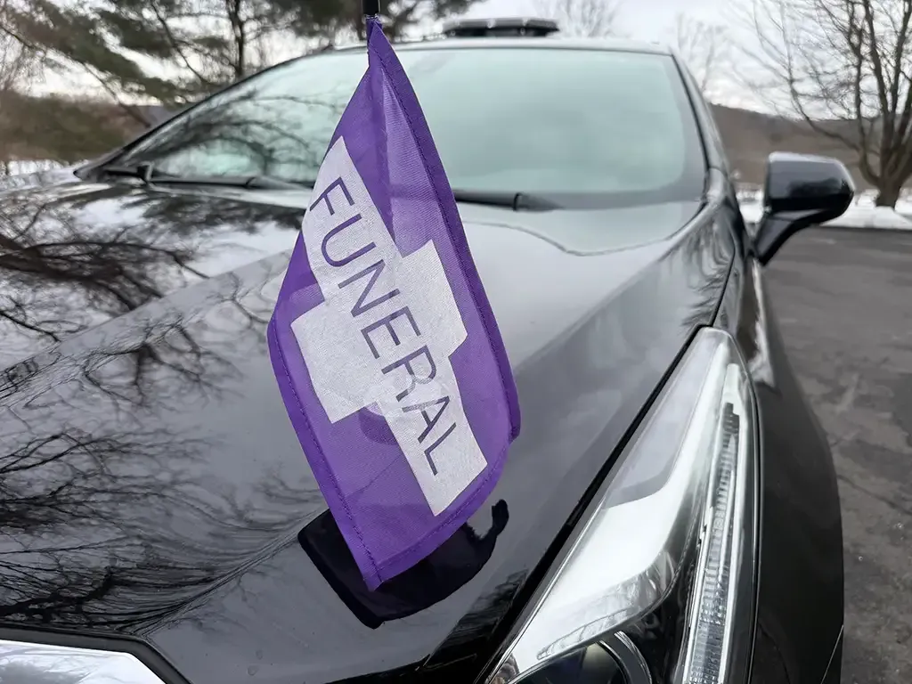 Purple funeral flag on the hood of a black car parked outdoors in winter.