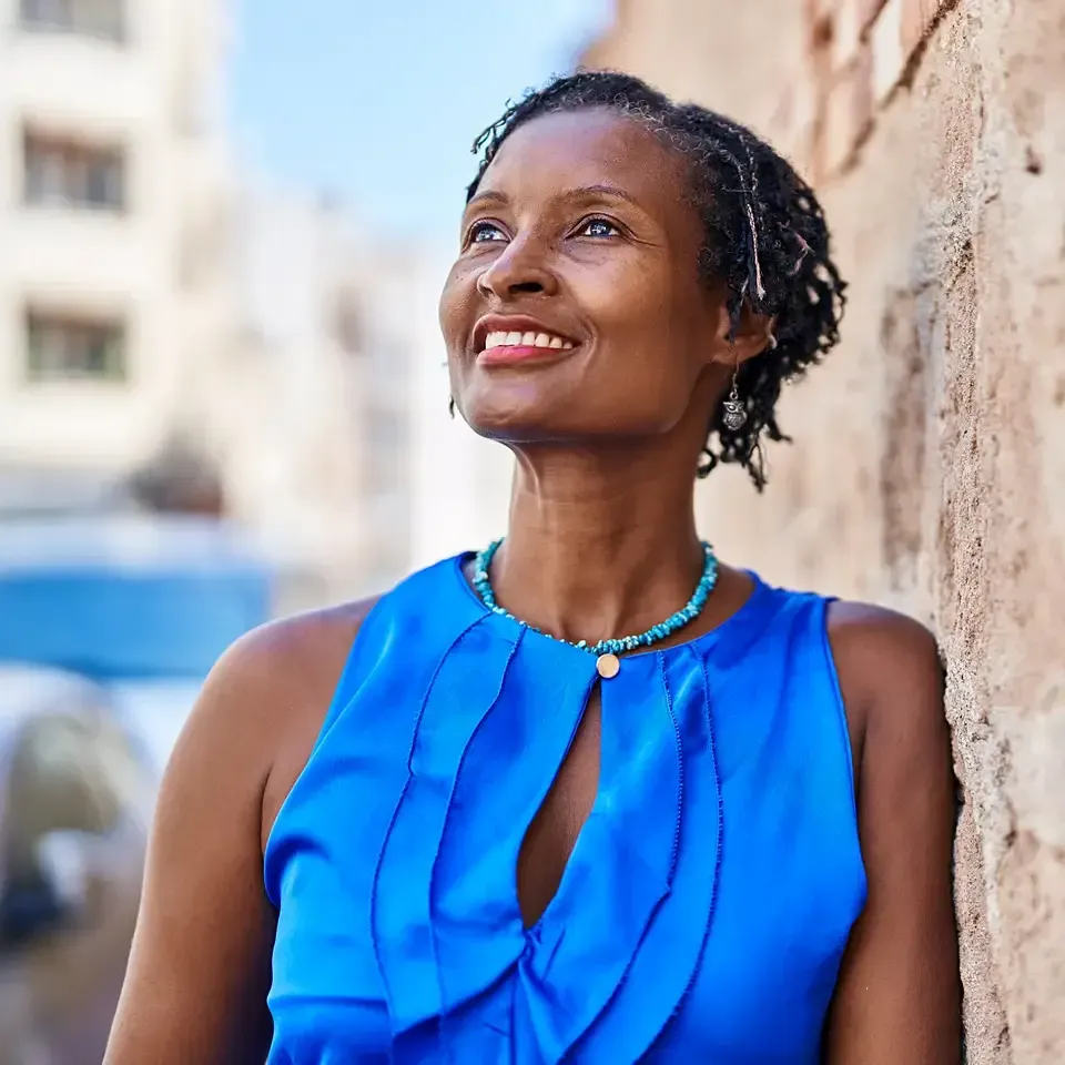 Smiling person in a bright blue sleeveless top looking upward beside a wall