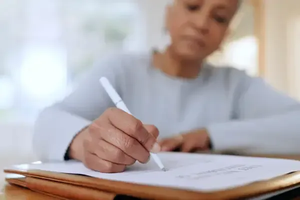 Person writing in a notebook at a desk with a white stylus, in a softly lit room