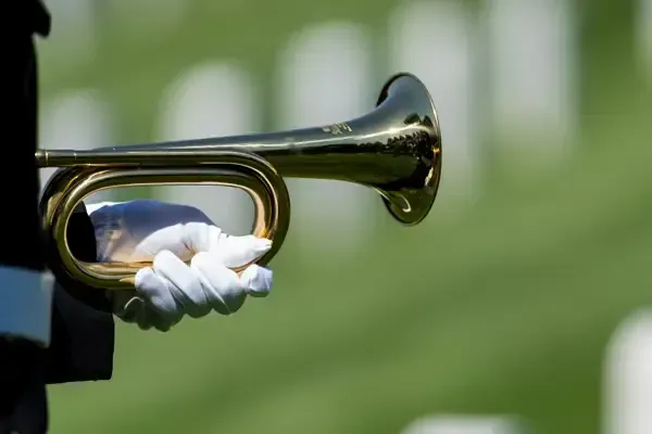Close-up of a brass trumpet held by a white-gloved hand against a blurred green background