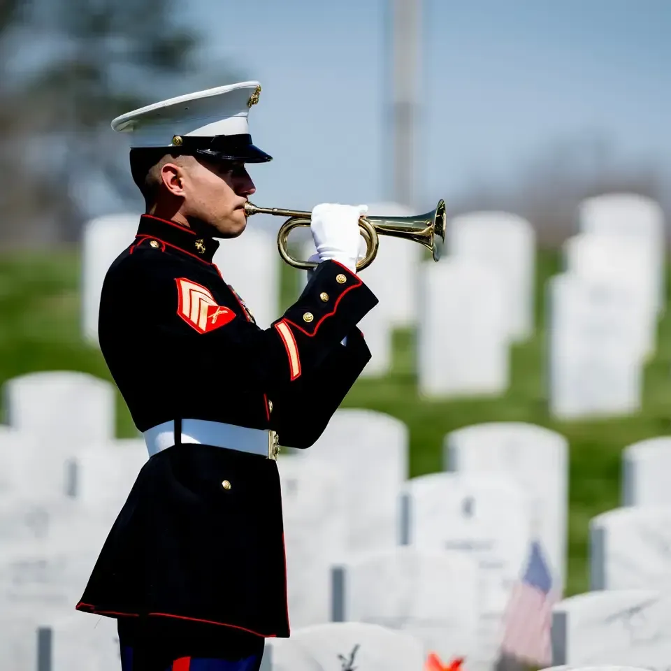 Marine bugler in dress uniform playing at a cemetery with white headstones in the background