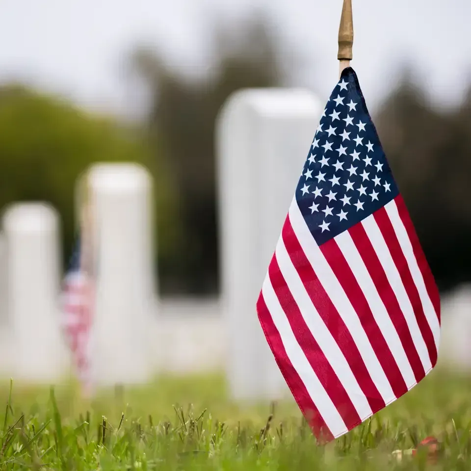 American flag planted in grass with blurred white headstones in the background