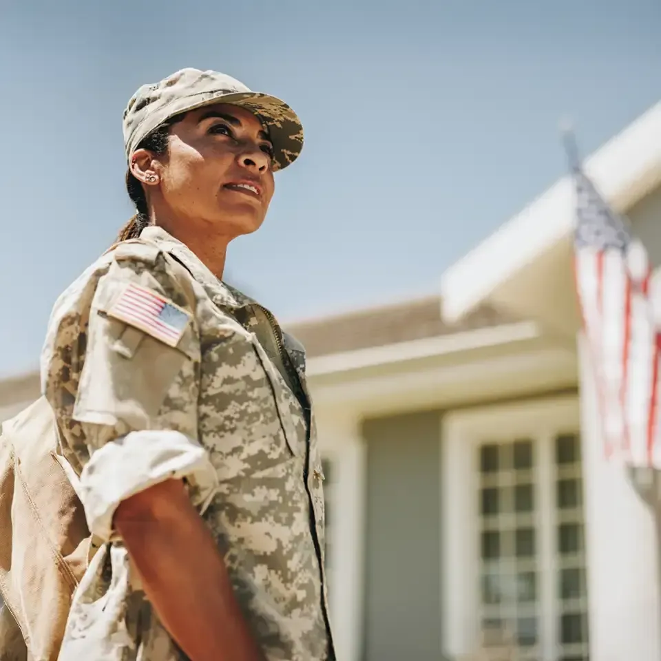 Uniformed soldier standing outdoors in front of a building, looking upward in bright sunlight