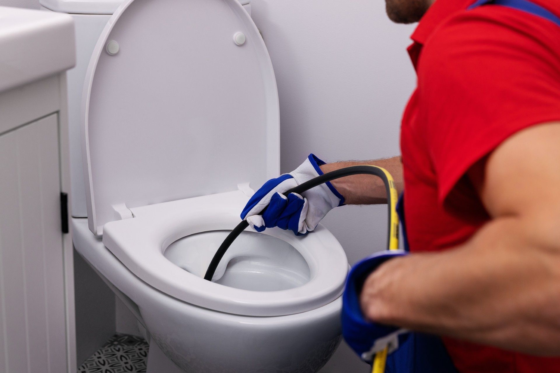 A man is fixing a toilet with a hose in a bathroom.