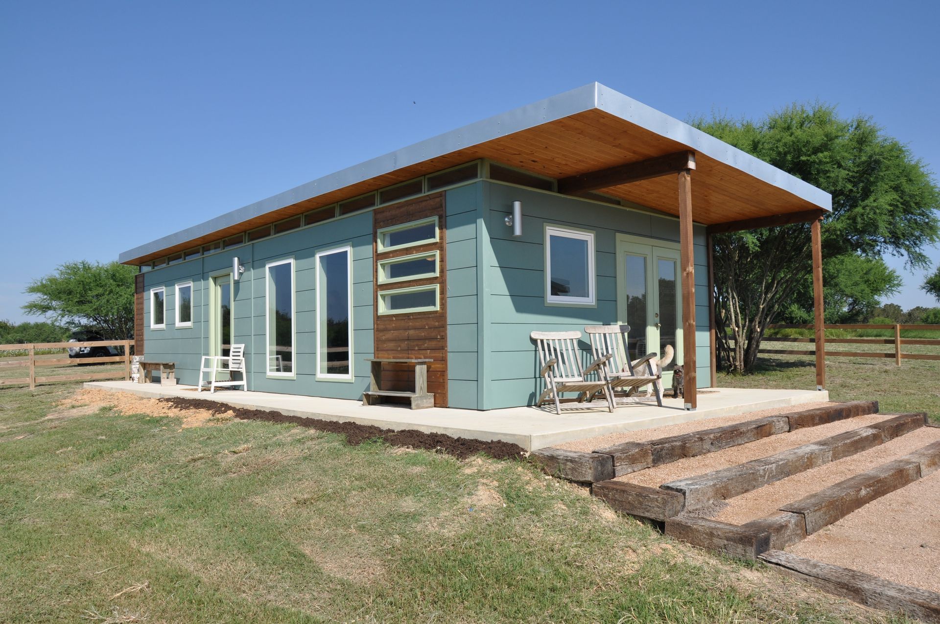 Modern grey shed with light blue doors and windows, on a green lawn with trees.
