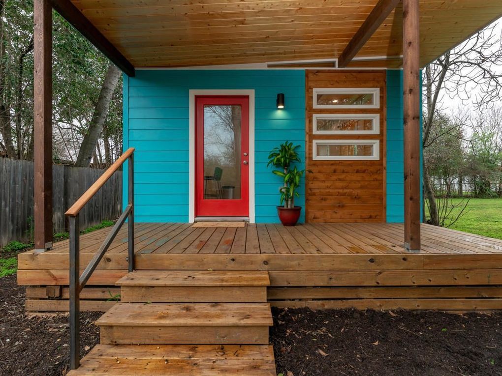 Tiny turquoise home with red door, wooden porch and steps, and a cedar-covered overhang.