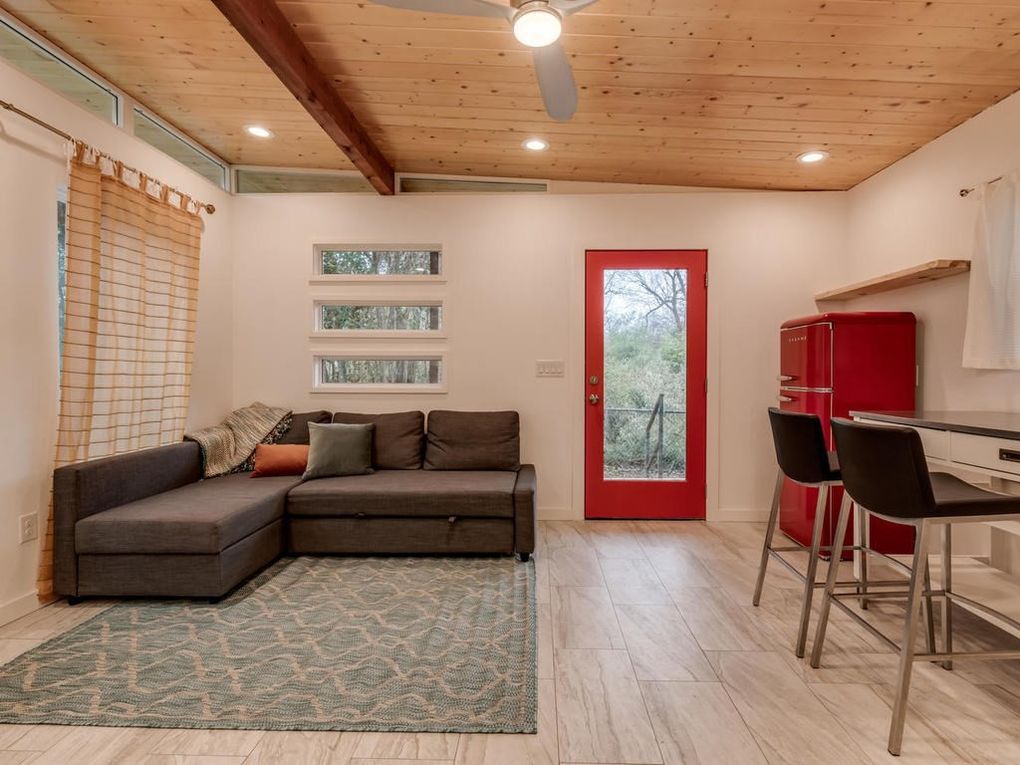 Cozy living area with a gray sectional, red door and refrigerator, and a wood ceiling.