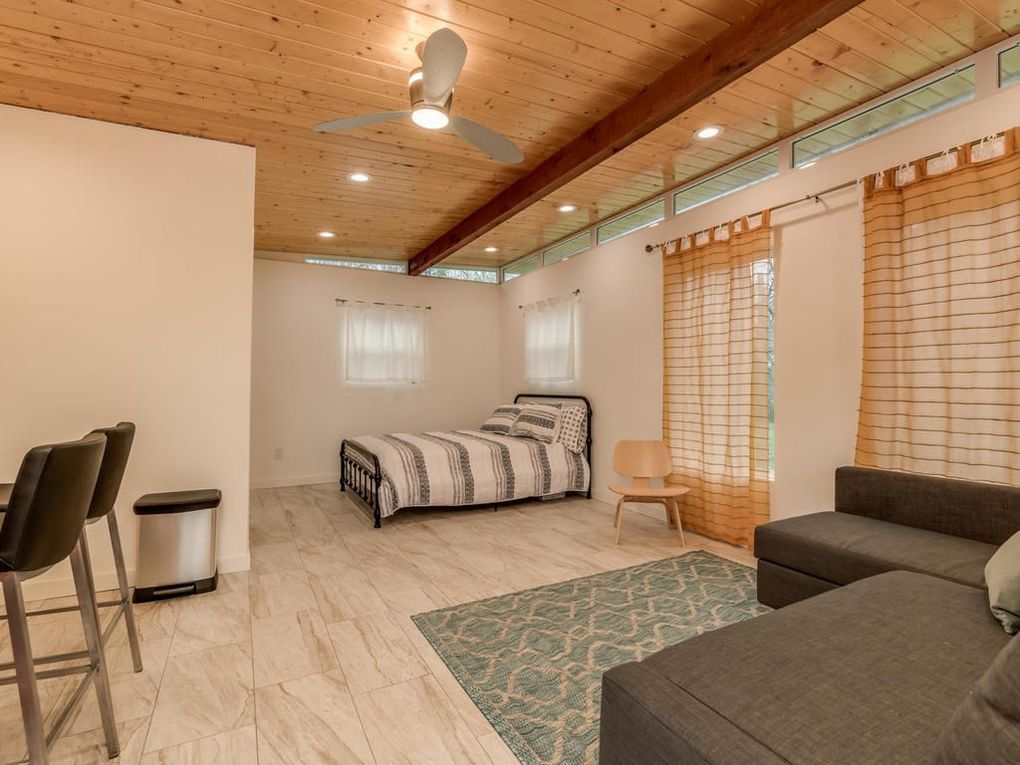 Spacious interior with bed, couch, and bar seating under a wood-paneled ceiling. Bright and airy space with neutral tones.