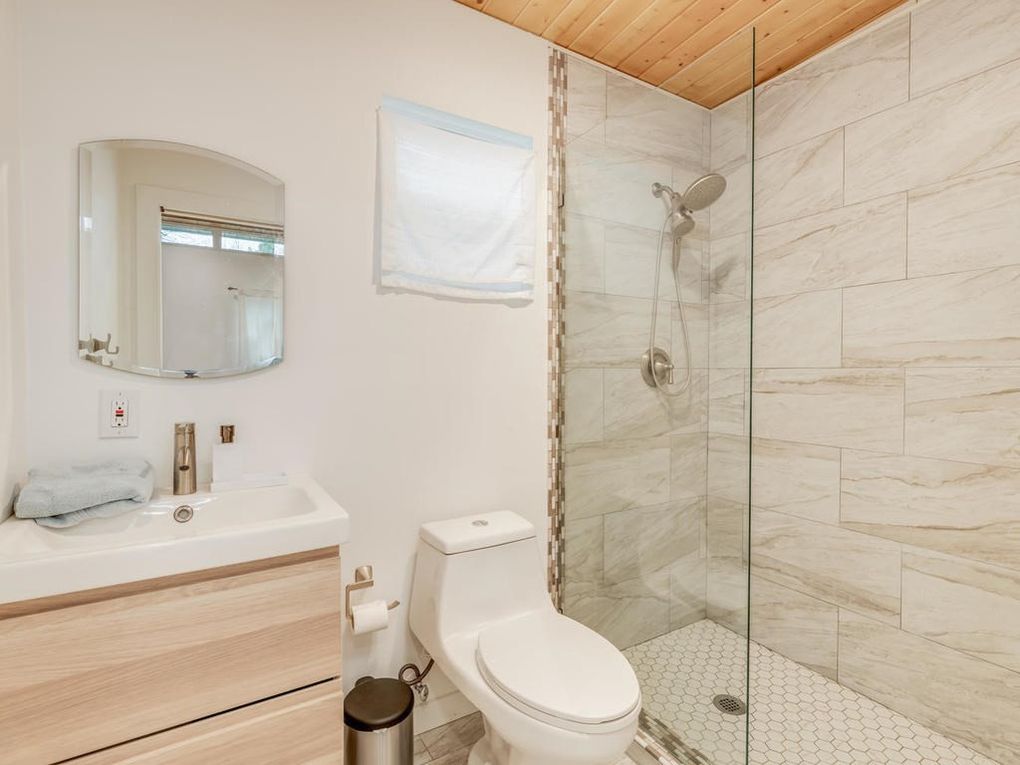 Bathroom with a white toilet, shower with glass door, vanity with mirror.