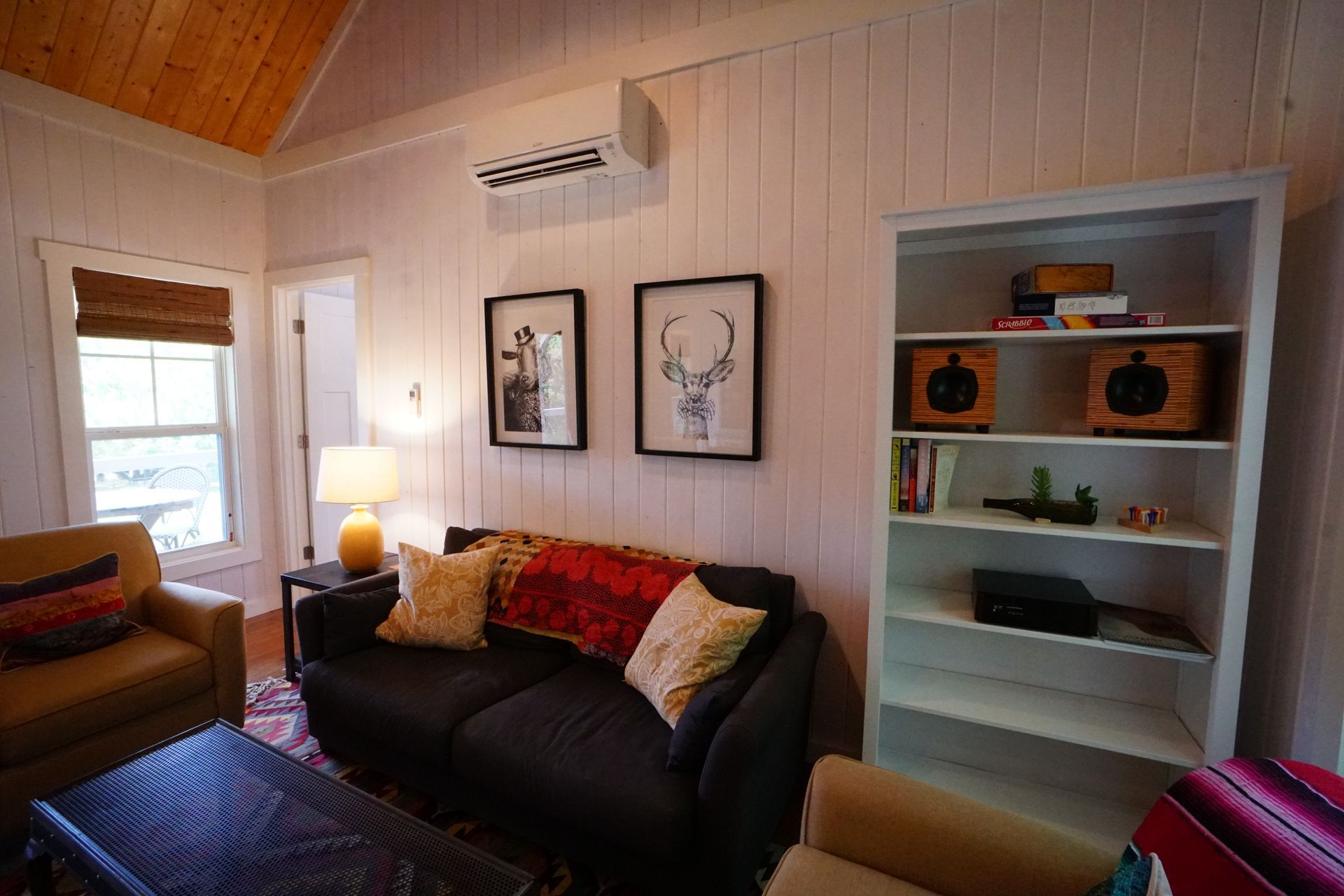 Cozy living room with a couch, armchair, bookshelf, and artwork on white paneled walls.