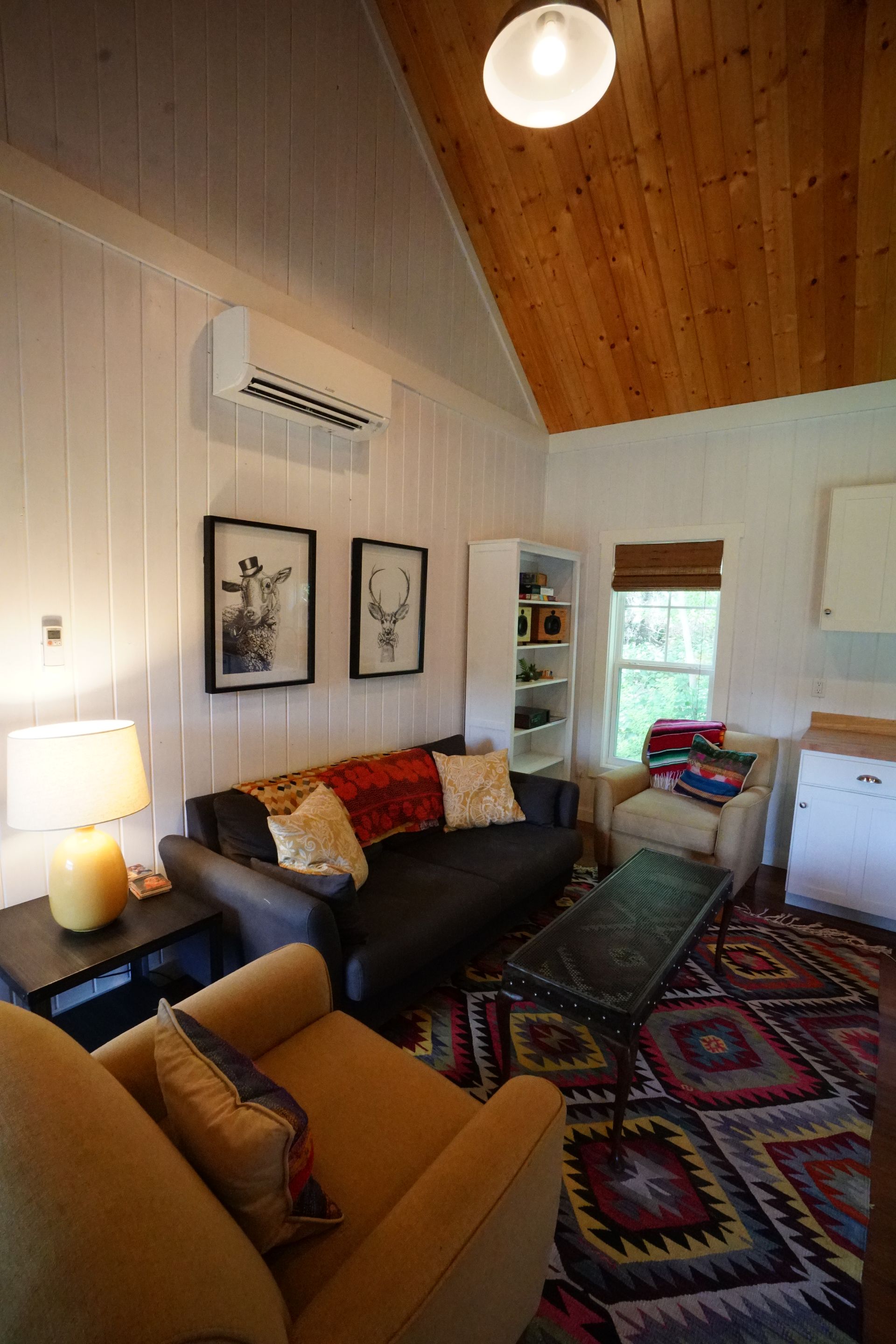 Cozy living room with a black sofa, colorful rug, white walls, and wood ceiling.