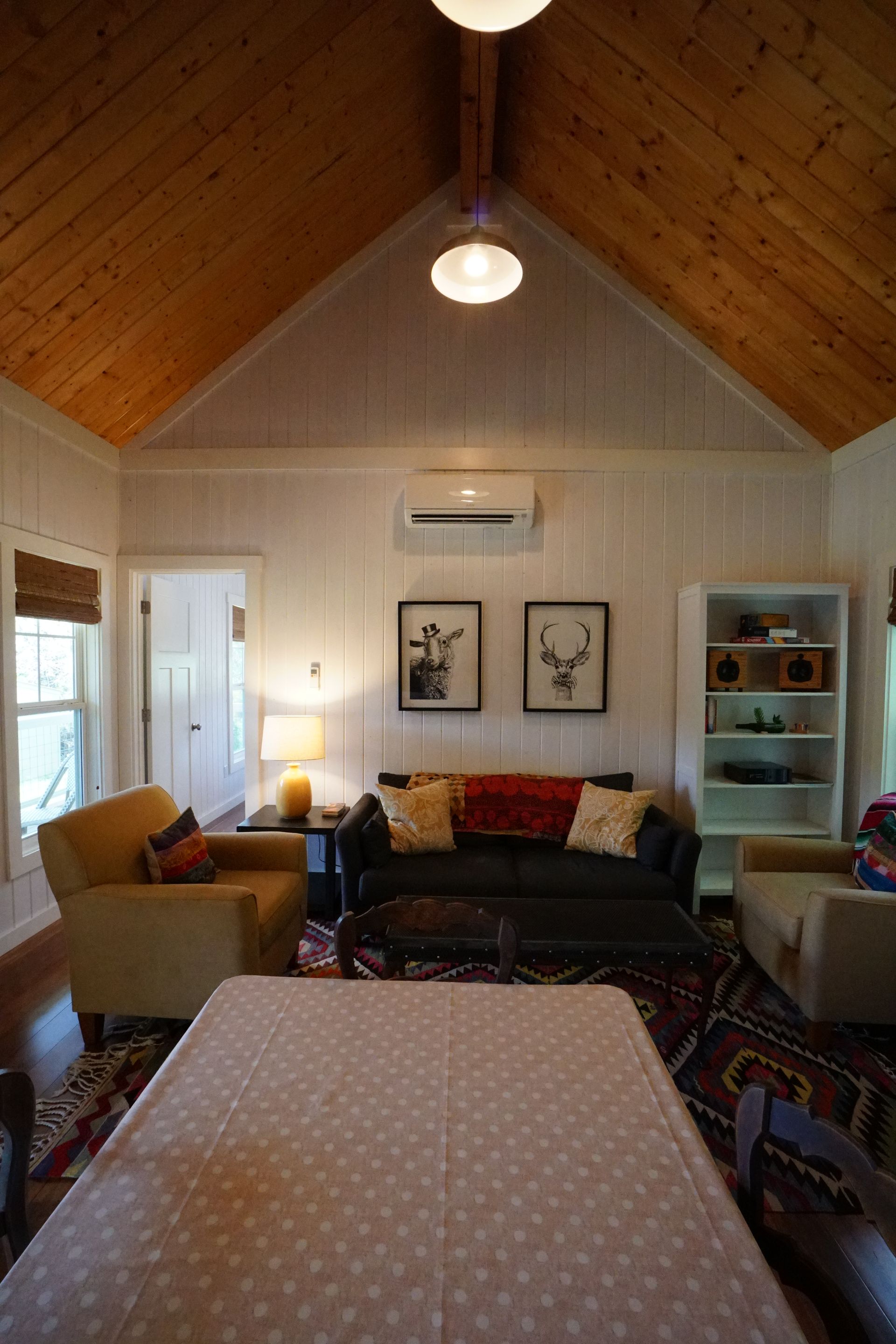 Cozy living room with vaulted wood ceiling, white walls, sofa, armchairs, and framed art.