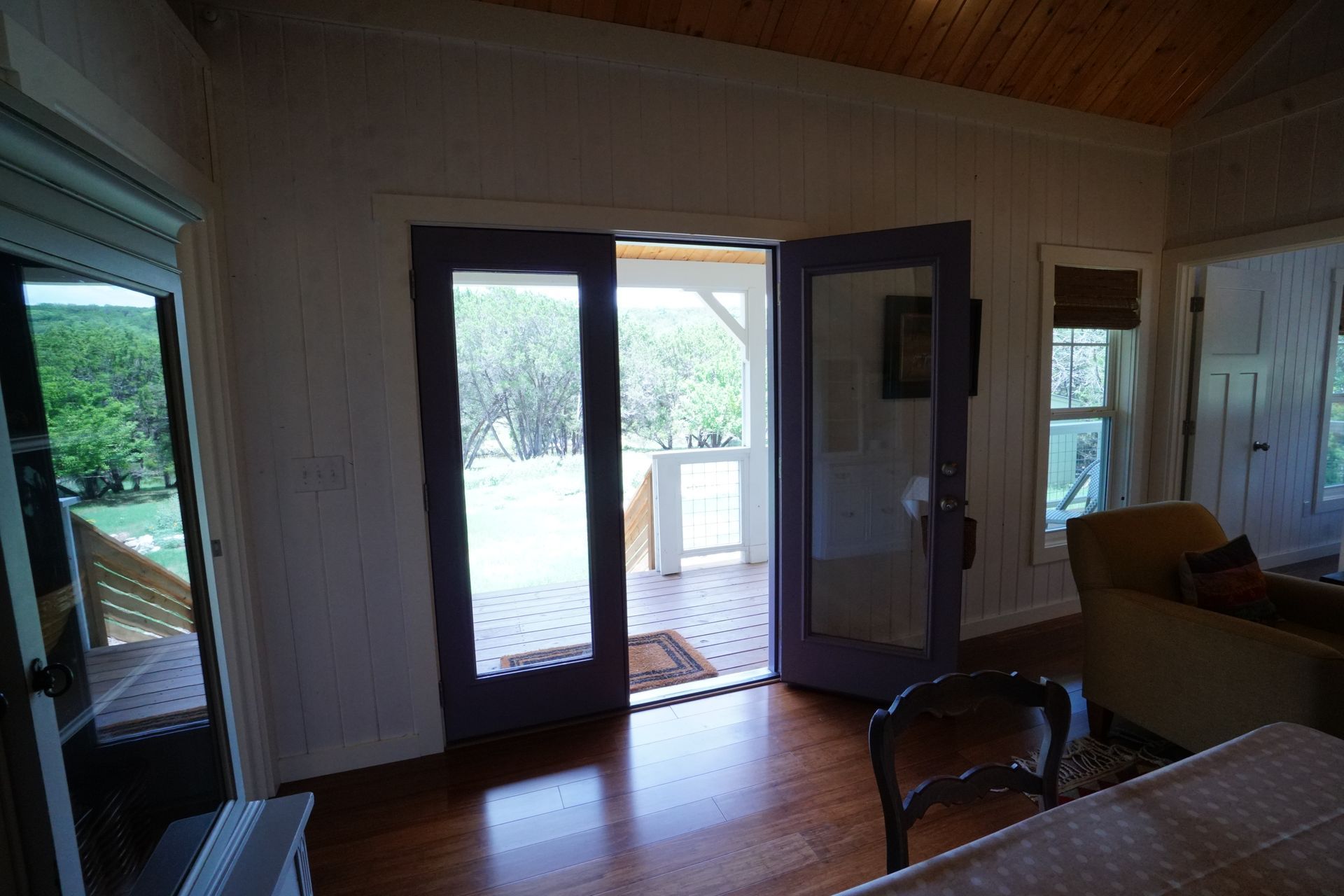 Interior view with French doors leading to a porch. Purple door frames, wood floor, white walls.