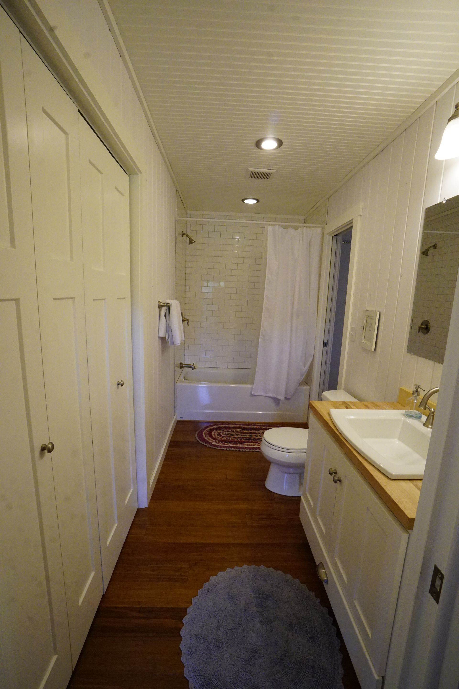 Bathroom with white vanity, toilet, and shower/tub. Hardwood floors and white paneled walls and ceiling.