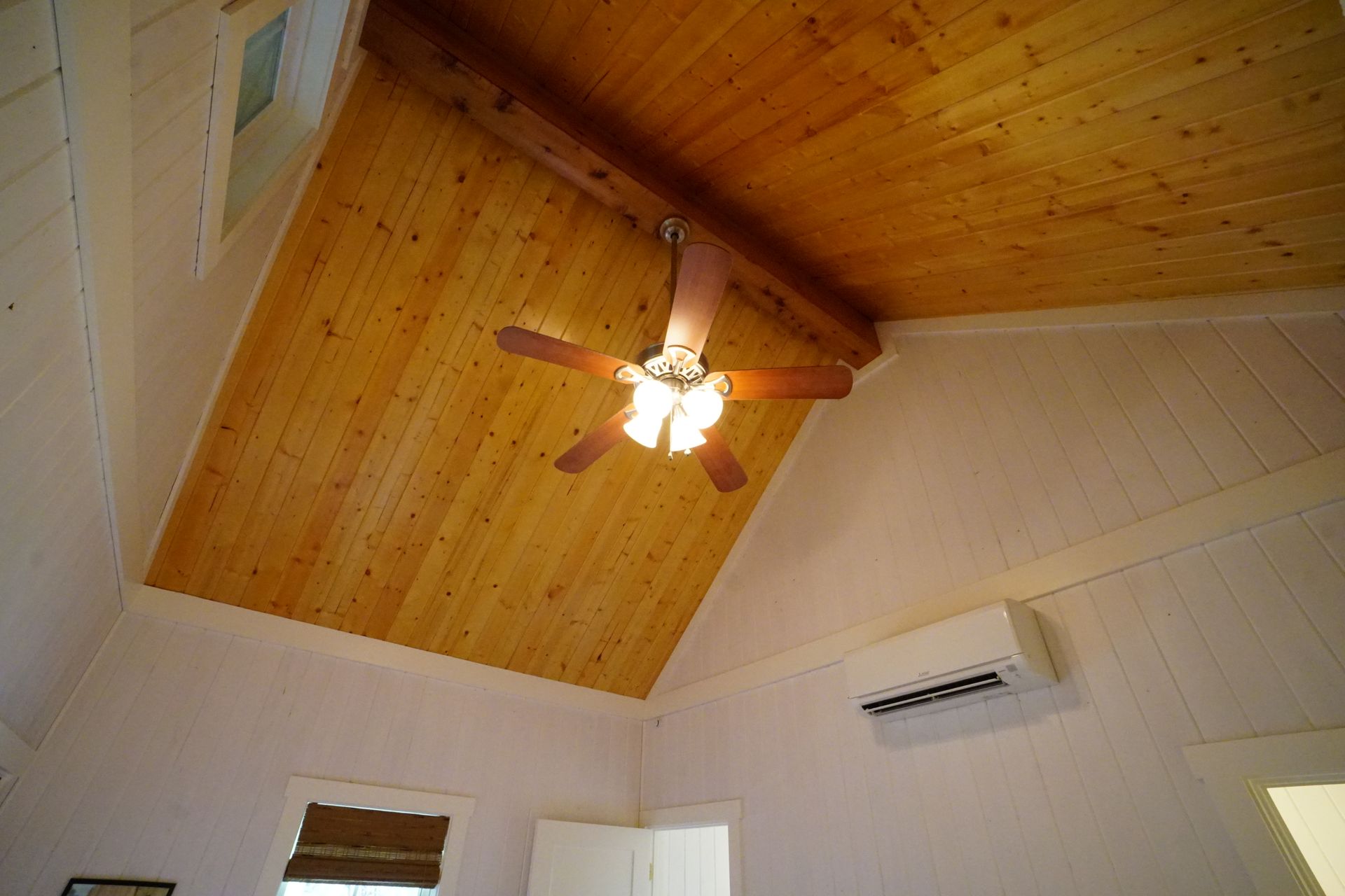 Wooden sloped ceiling with ceiling fan and white walls.
