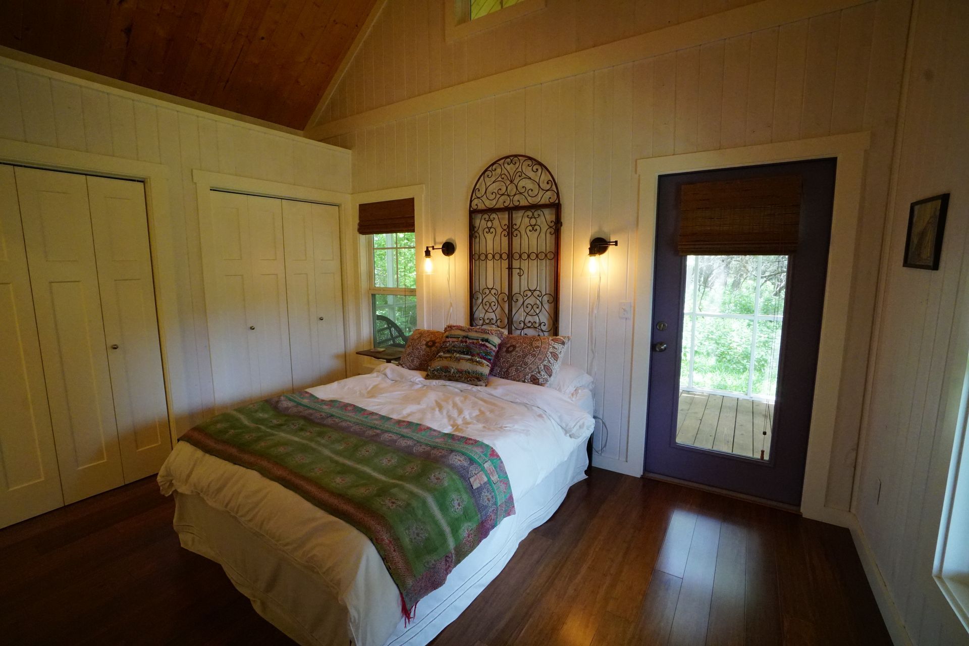 Bedroom with a bed, white walls, wood floor, and a door leading outside.