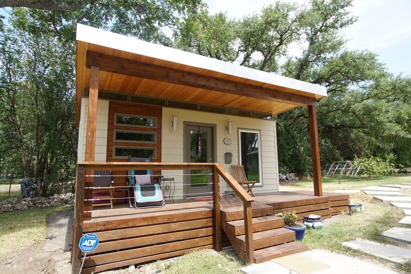 A small house with a porch and stairs is surrounded by trees.