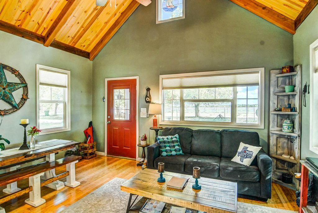 Cozy living room with dark green walls, wood ceiling, red door, couch, and rustic decor.